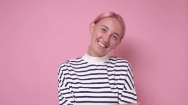 Çekici gülüşü ve boyalı pembe saçı olan kadın kameraya bakıyor.