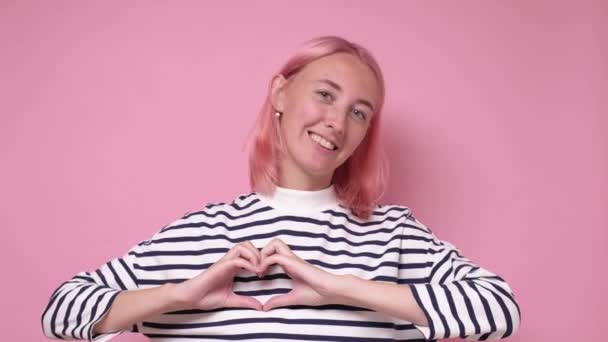 Fiatal kaukázusi nő rózsaszín festett haj mutató szív gesztus a kezét — Stock videók