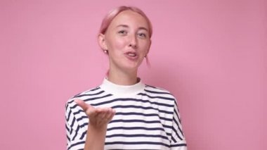 Pembe saçlı beyaz bir kadın pembe arka planda hava öpücüğü yolluyor..