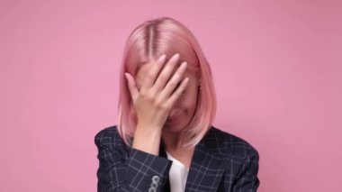 Pembe boyalı saçlı bir kadın yüz hareketi yapıyor, sıkılmış hissediyor.