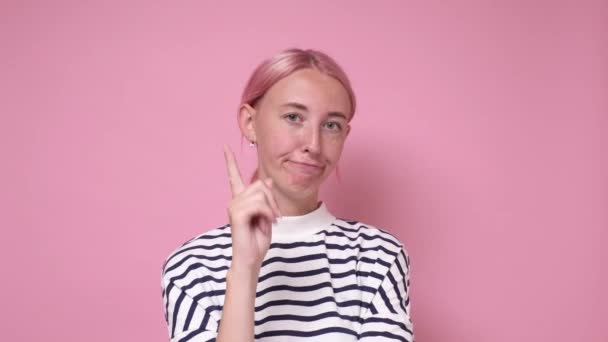 En ung kvinna viftar med fingret och grälar med sin pojkvän. Studio skjuten på rosa vägg. — Stockvideo