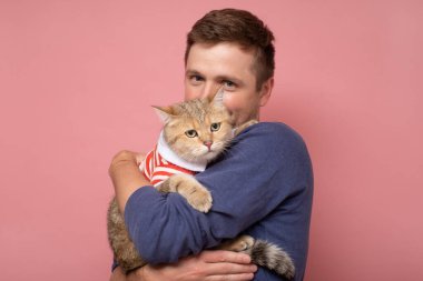 İngiliz tekir kedisi olan beyaz bir genç adam pembe arka planda izole edilmiş..