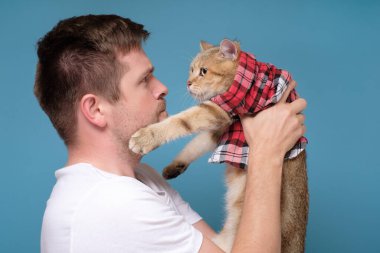 Kafkasyalı genç bir adam İngiliz bir kedi tutuyor ve şaka yaptığı için onu azarlıyor.
