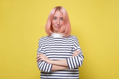 Kendinden emin gülümseyen, pembe saçlı, elleri katlanmış genç bir kız öğrenci.