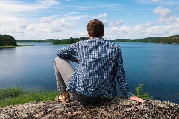 Hombre sentado en una colina mirando el agua del lago. — Foto de Stock