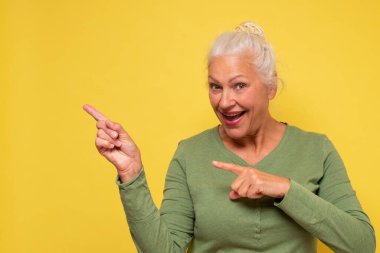 Üst düzey bir kadın, mekanı işaret ediyor. Stüdyo fotoğrafı sarı duvarda..