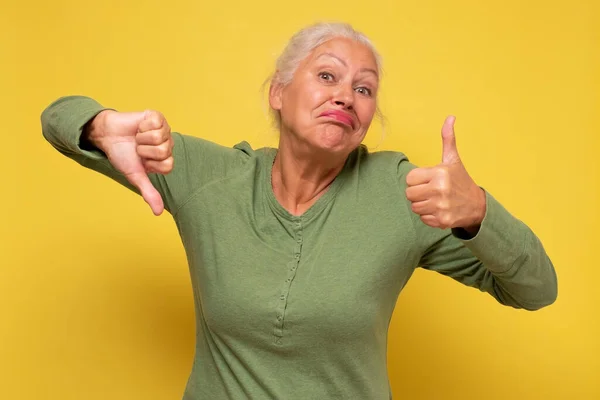 Senior italian woman showing thumbs up and down trying to make a decision.