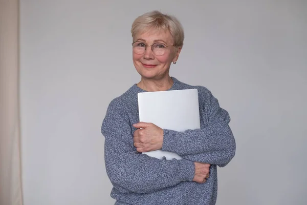 Зрелая женщина в очках держит ноутбук и улыбается. — стоковое фото