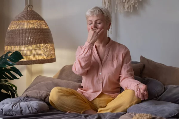 Mujer mayor practicando yoga en casa, haciendo ejercicio de respiración nasal alternativa, nadi shodhana pranayama — Foto de Stock