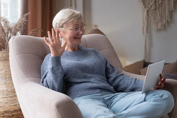 Senior kvinna använder surfplatta sittandes hemma chatta med vänner — Stockfoto