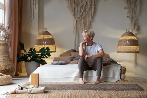 Retrato de mujer mayor en la cama después del yoga y mirando a la ventana — Foto de Stock