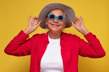 Güneş gözlüğü takan neşeli yaşlı kadın, sarı arka planda izole edilmiş kahkahalar atıyor..