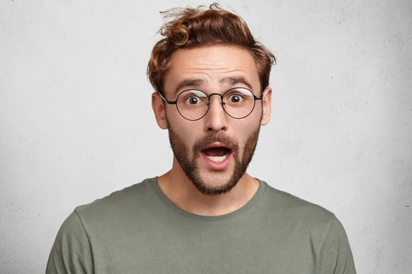 bug eyed hipster man or clever student in casual t-shirt, screams in shock, keeps mouth wide open, feels stressful.