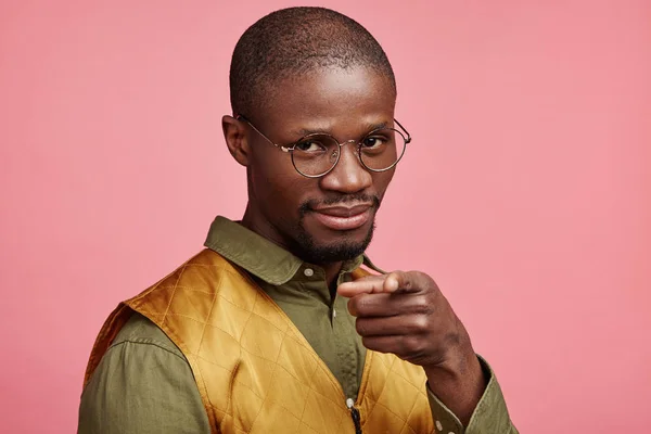 I choose you. Serious male with mustache, beard and dark skin, points fore finger at camera, looks confidently, isolated over pink background. African guy selects someone or advertises something