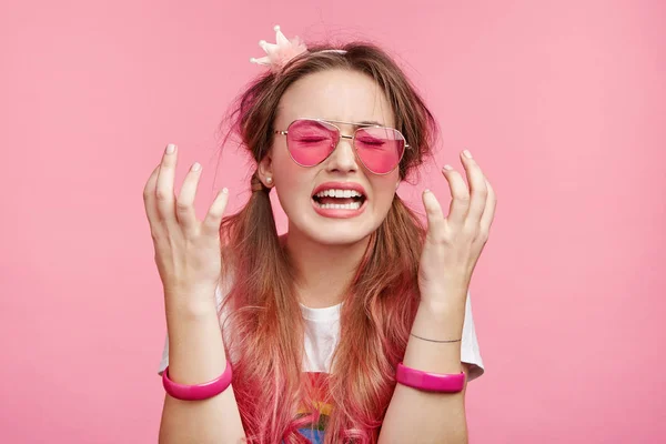 Desperate female wears pink glasses, gestures in puzzlement, being depressed as has no money for going shopping, cries in despair, doesn`t know how improve situation.