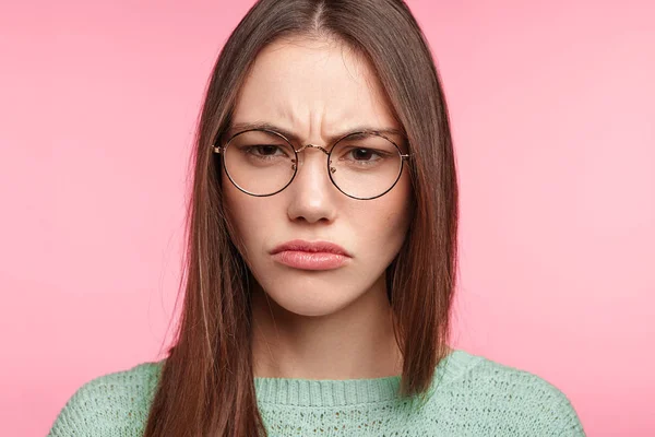 Portrait of discontent dissatisfied brunette female frowning face in dissatisfaction on pink background