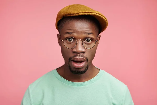 Headshot of emotional excited black man stares at camera with disbelief, can`t understand or belief in his big failure at international competition, amazed with cool news, says omg poses over pink wall
