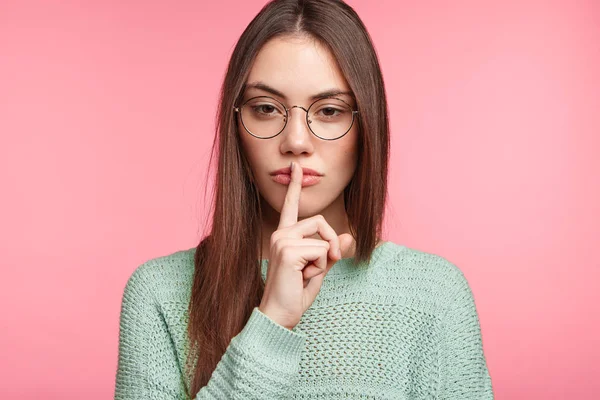 Serious female asking to keep confidential information in secret on pink background