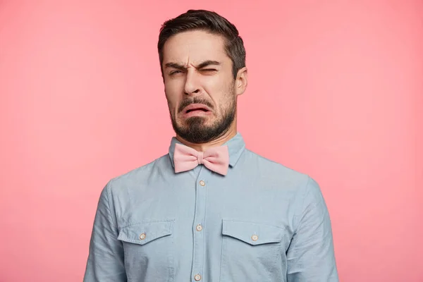 Ugh, how disgusting! Displeased unshaven young male dressed formally, says fie and has dissatisfied facial expression as sees something abominable or detestable, isolated over pink studio background