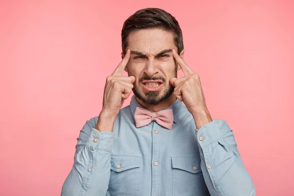 Brunet discontent handsome young male model with trendy hairdo frowns face in displeasure, being forgettable, fails to concentrate as has terrible headache after conference, dressed formally