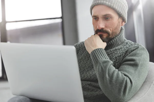 Confident bearded office manager watches database on modern laptop computer, reads something with serious concentrated expression.