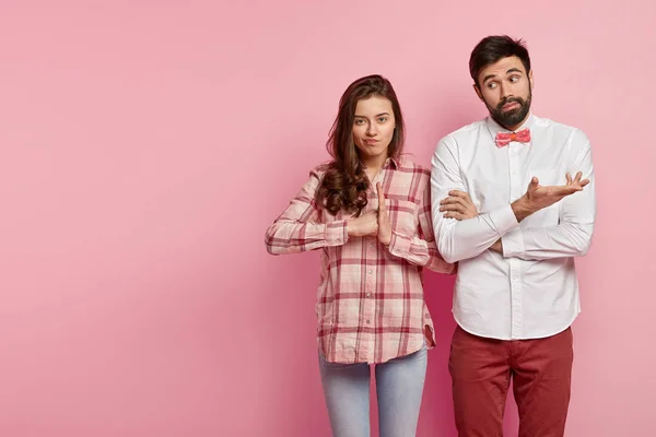 Dissatisfied angry woman clenches fist, confused bearded man gestures with hesitation, express different emotions and feelings, isolated over pink background with free space away.