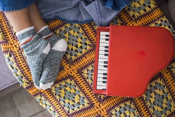 woman relaxed feet with nice socks at home in rest position. little piano toy on the sofa near her. music and artist life with pattern cover with vintage colors and background. lifestyle happy at home