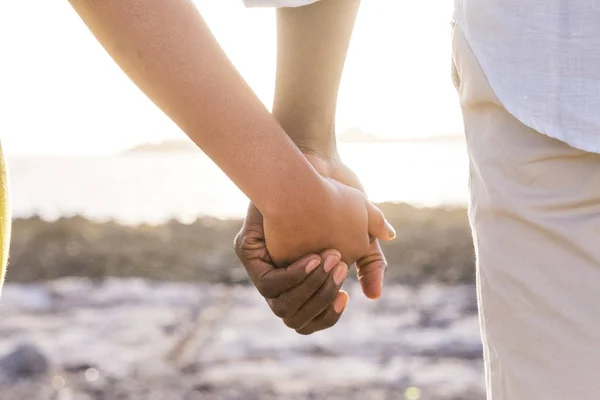 特写的两个恋人的手留在一起 夕阳背光在背景遥远 爱和柔情在海滩上为男人和女人年轻的黑人种族 生活永远团结理念 — 图库照片