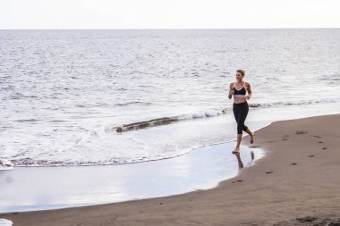 Siyahlısı sahilde yalnız kız sarışın koşucu. sağlıklı ve güzel vücut ile kalmak sabah etkinliği. yalınayak koşmak sahilde koşu ve ayak basacak etkinliği açık kavramı