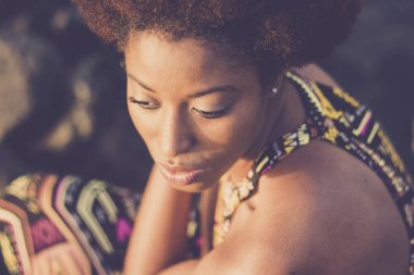 güzel siyah ırk portre Afrikalı model genç kadın kalmak otur ve Okyanusu yakın deniz kenarı hakkında düşünüyorum. yüzü ve eski stil saç üzerinde güneş ışığı. geleneksel elbise ve güzellik kavramı