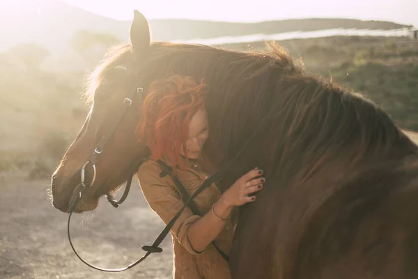red hair beautiful caucasian womanhug with love his best friends horse under the sunset outdoot in backlight. friendship and relationship animals therapy concept and alternative lifestyle