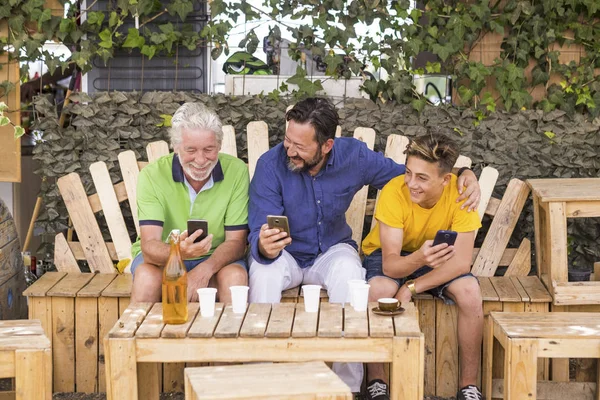 family generations men with grandfather father and son nephew from old to young stay together using cellular technology smartphone to connect to internet and check modern related concepts. caucasian people outdoor leisure concept