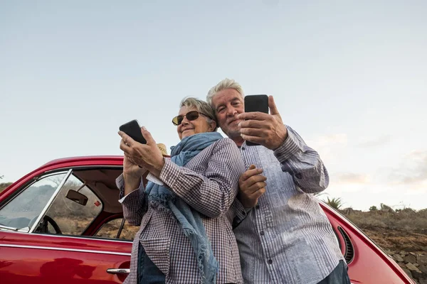Mutlu yaşlı üst düzey çift cep telefonları kırmızı güzel bir retro araba açık kullanın. boş zaman etkinliği ve seyahat birlikte sonsuza kadar kavramı. Modern hayat zevk eski yetişkin teknoloji kullanımı