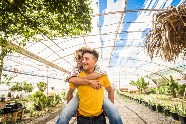 young beautiful teenager play with his mother middle age pretty woman carrying her to his back. couple mother son having fun together like a perfect family in outdoor leisure activity. happy people concept