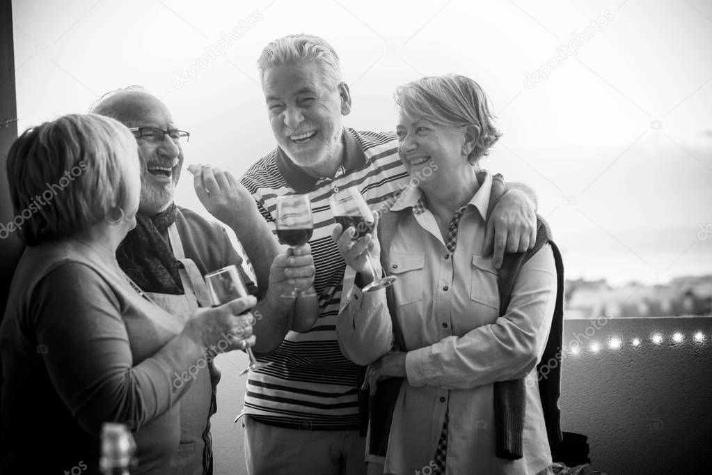 group of 4 seniors, two couples, stay togheter and have fun enjoing a cup of wine outdoor in the rooftop. vacation elderly concept and friendship. sunlight anche clear sky