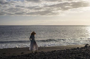 Siyahlısı sahilde yürüyüş yalnız güzel orta yaş Bayan seyahat. siyah taş ve kum volkanik doğal yer. arka plan ve altın günbatımı ışık Adaları