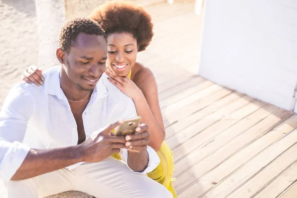 beautiful couple of black race african models use the smartphone together in friendship smiling and enjoying the contents. connected with friends or looking at the pics. love friends couple concept