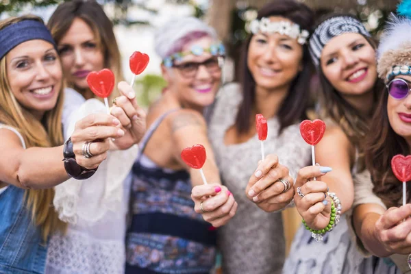 group of mixed ages women from young to old stay together in friendship taking and offering a candy hearth lollipops to you. peaceful and lifestyle inspired to peace and love like hippy style