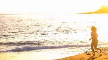  koşma ve atlama kumsalda altın bir muhteşem gün batımı sırasında rahat güzel kadın. Tatil ve yaşam tarzı açık hava etkinliği konsepti ile plaj zevk modeli