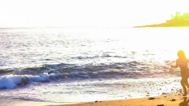 リラックスした美しい女性の実行している黄金の素晴らしい夕日の中にビーチでジャンプします モデルではビーチを楽しむ休暇とライフ スタイルの屋外活動の概念 — ストック動画