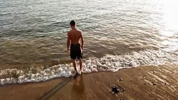 英俊的白种青少年与肌肉在15岁的海滩上寻找地平线和享受金色的夕阳在背景下 — 图库视频影像