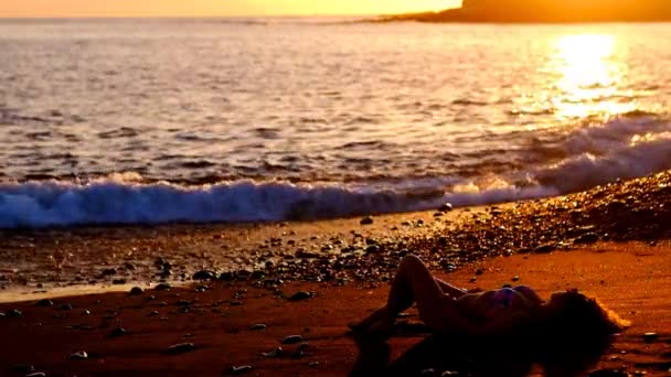 黄金の素晴らしい夕日の中に海の波の近くの砂の上リラックスした美しい白人女性を置きます モデルではビーチを楽しむ休暇とライフ スタイルの屋外活動の概念 — ストック動画