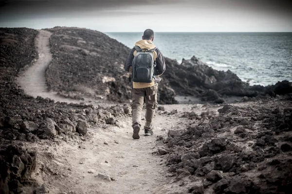 孤独的旅行者年轻人中年与徒步的衣服和背包走在海洋海岸线上的岩石沙漠 沿着一条海景之路 享受自由和另类生活方式 — 图库照片