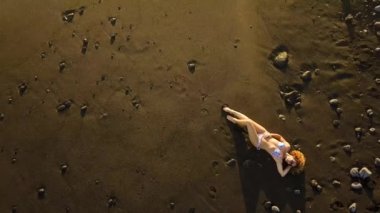 okyanus dalgaları yakınındaki kum üzerinde rahat güzel beyaz Bayan aşağı altın bir muhteşem gün batımı sırasında yatıyordu. Tatil ve yaşam tarzı açık hava etkinliği konsepti ile plaj zevk modeli