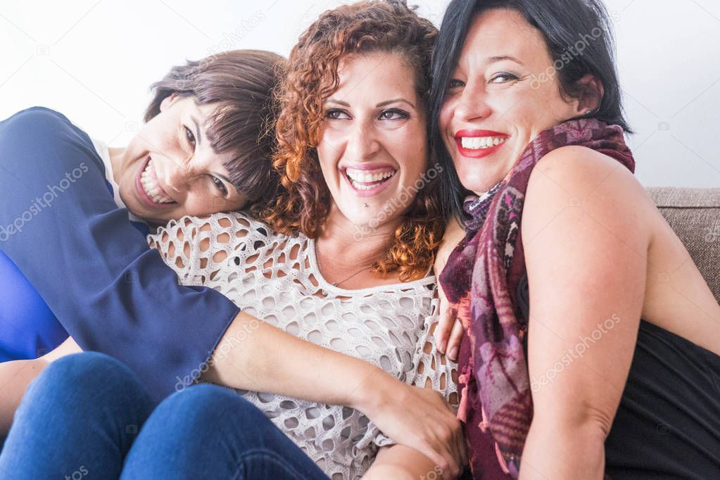 cheerful women sitting and hugging on sofa at home 