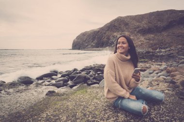 Genç kadın gündüz smartphone kullanırken sahil şeridi üzerinde rahatlatıcı