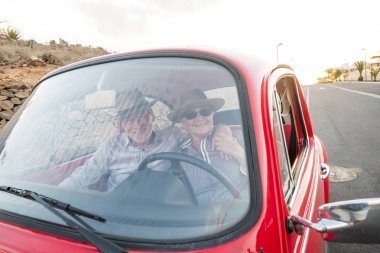 Elderly senior couple driving vintage red car during vacation  clipart