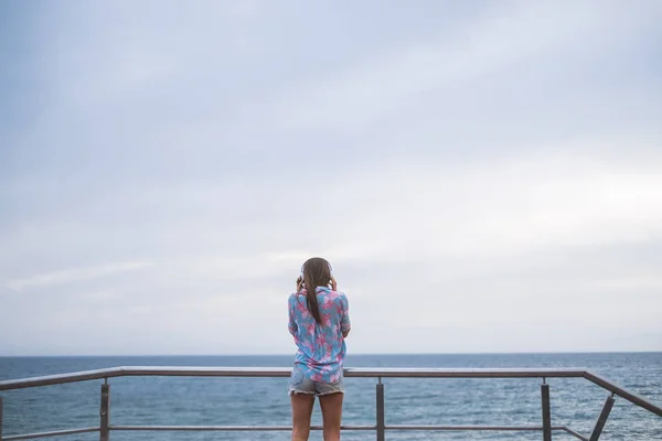 在欣赏海洋背景音乐的同时站在露台的年轻女子的后观 — 图库照片