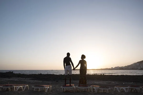rear view of couple standing on beach near sea on sunset background