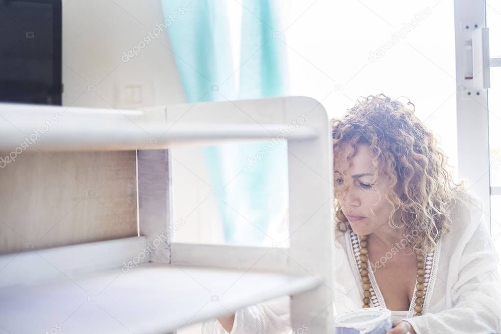 blonde curly young woman painting furniture in white color at home
